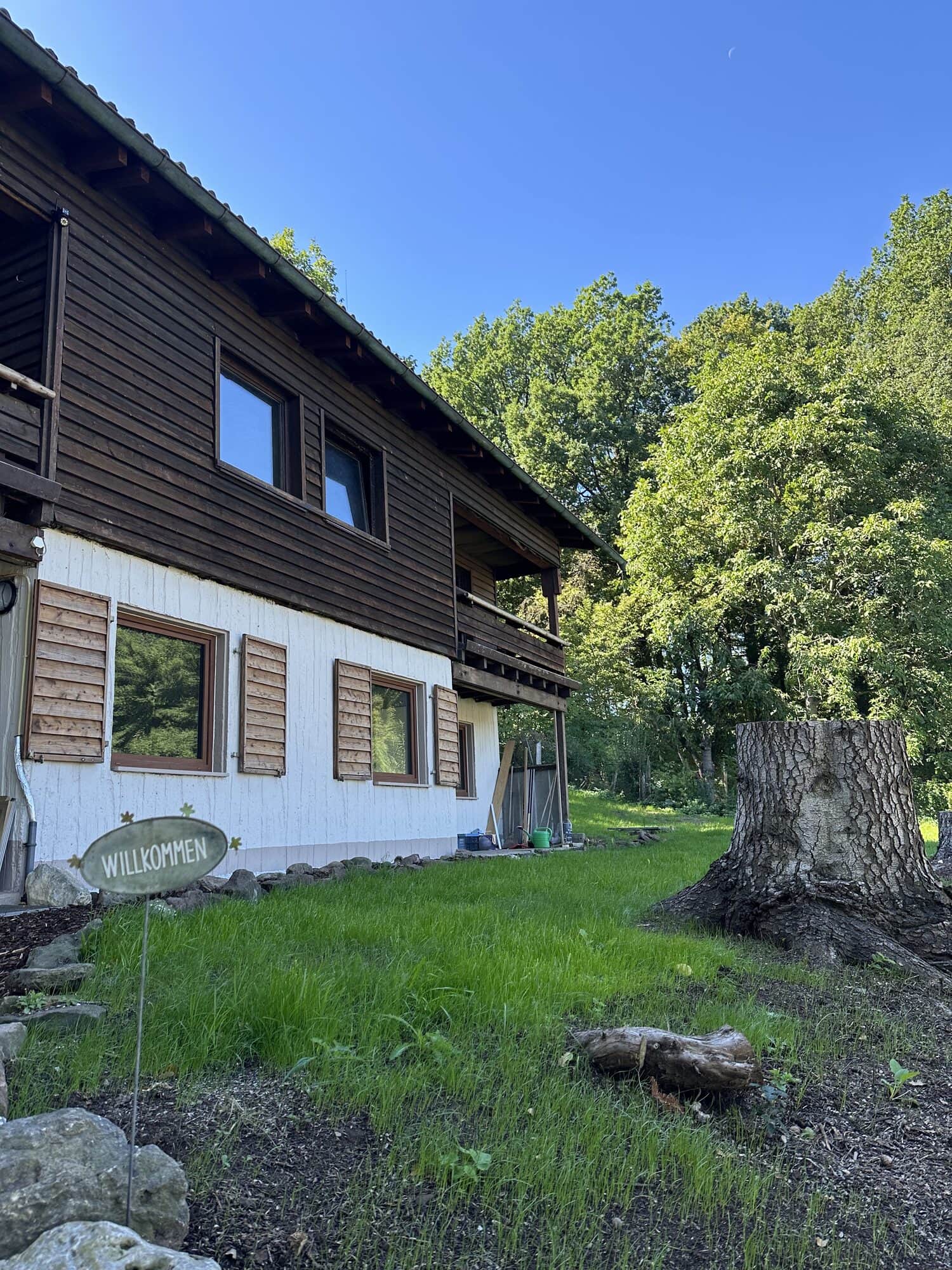 Ferienhaus Boxbrunn von außen: dunkles Holz, weiße Wand, Holzläden und Garten